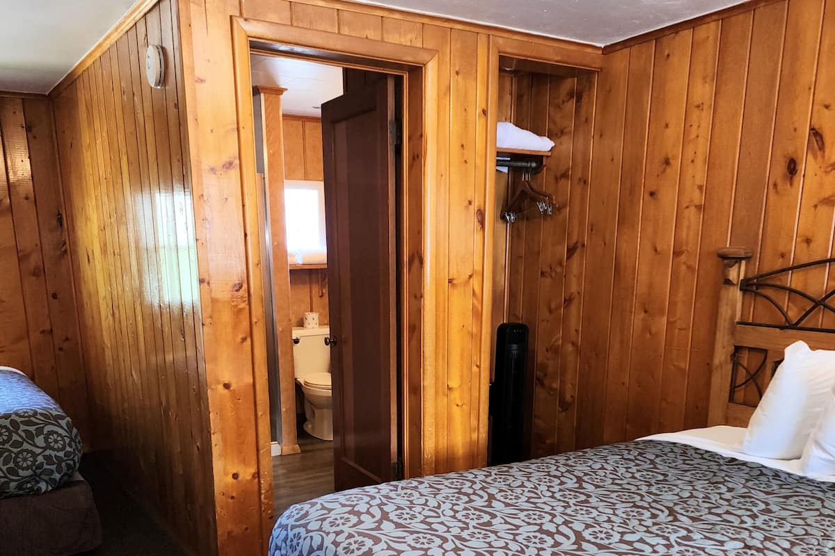 Ein Zimmer mit Holzboden, einem Bett, einer Tür zu einem Badezimmer und einer Wandleuchte.