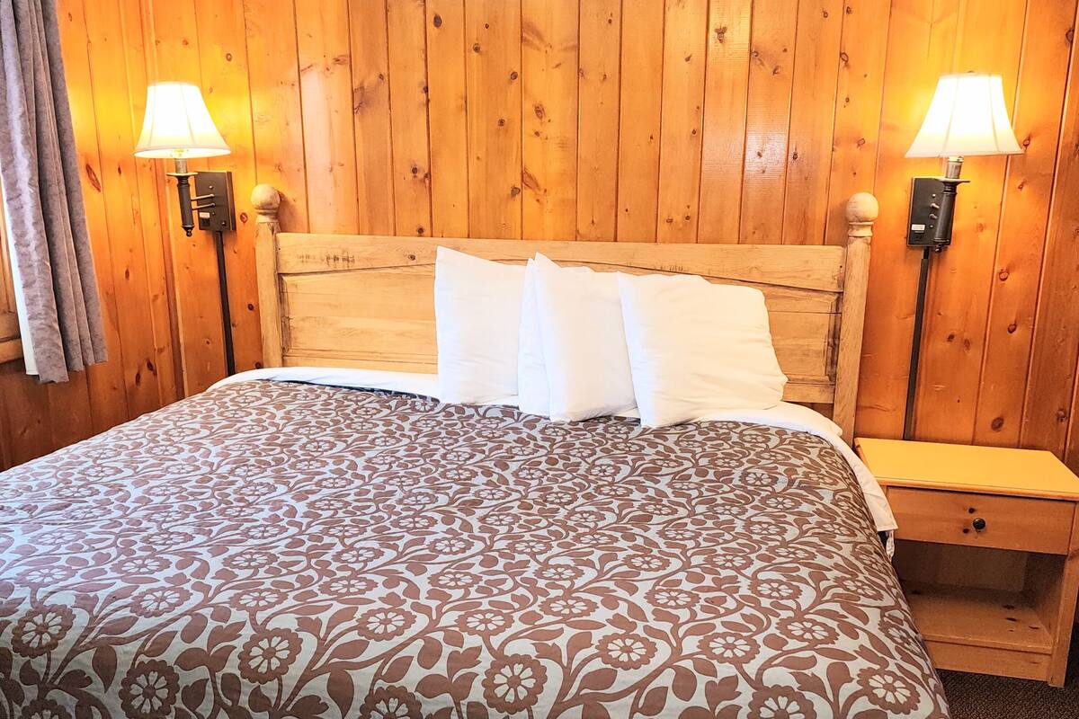 Ein Zimmer mit Holzwänden, einem Bett, zwei Nachttischlampen und einem Nachttisch.