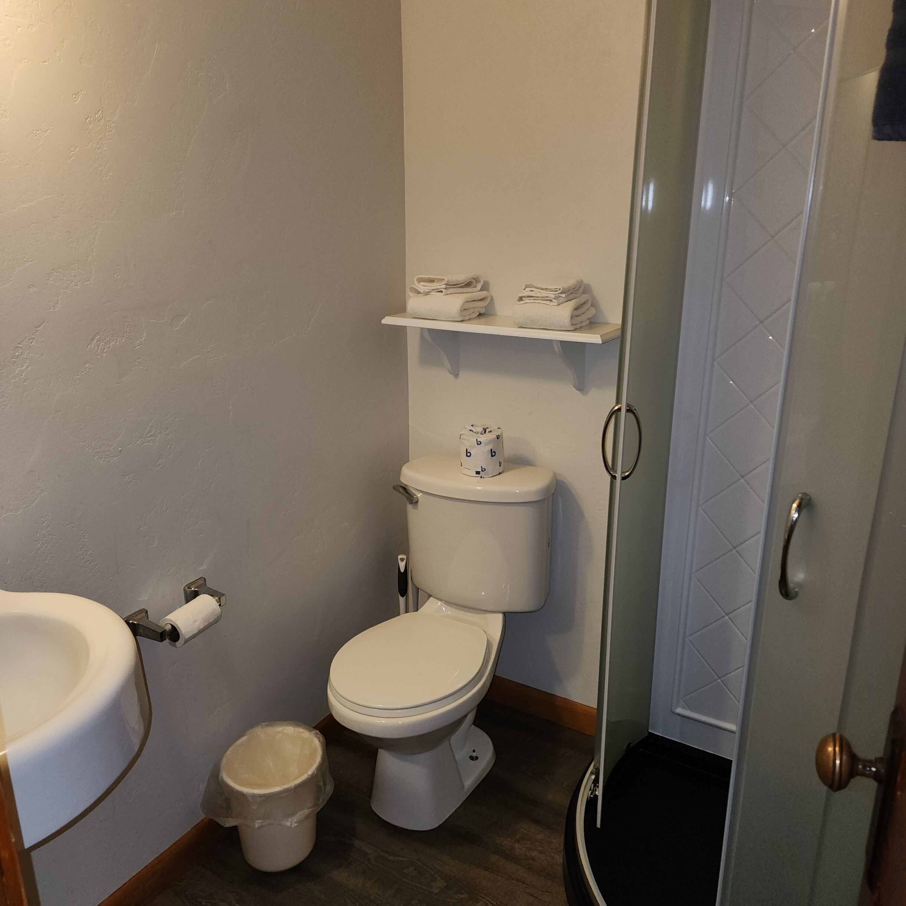 A bathroom with a toilet, sink, and a small trash bin. There is a towel rack above the toilet.