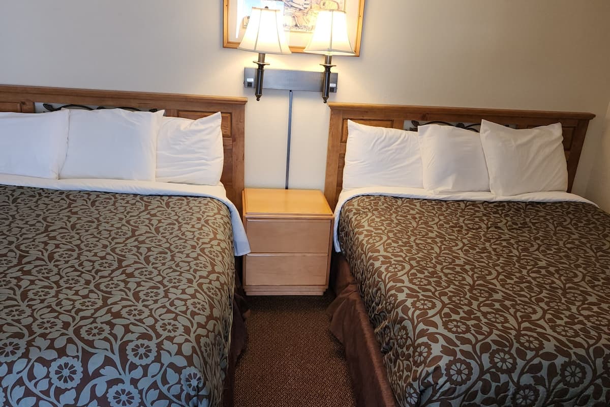 Ein Hotelzimmer mit zwei Betten, einem Nachttisch, einer Lampe und einem gerahmten Bild an der Wand.