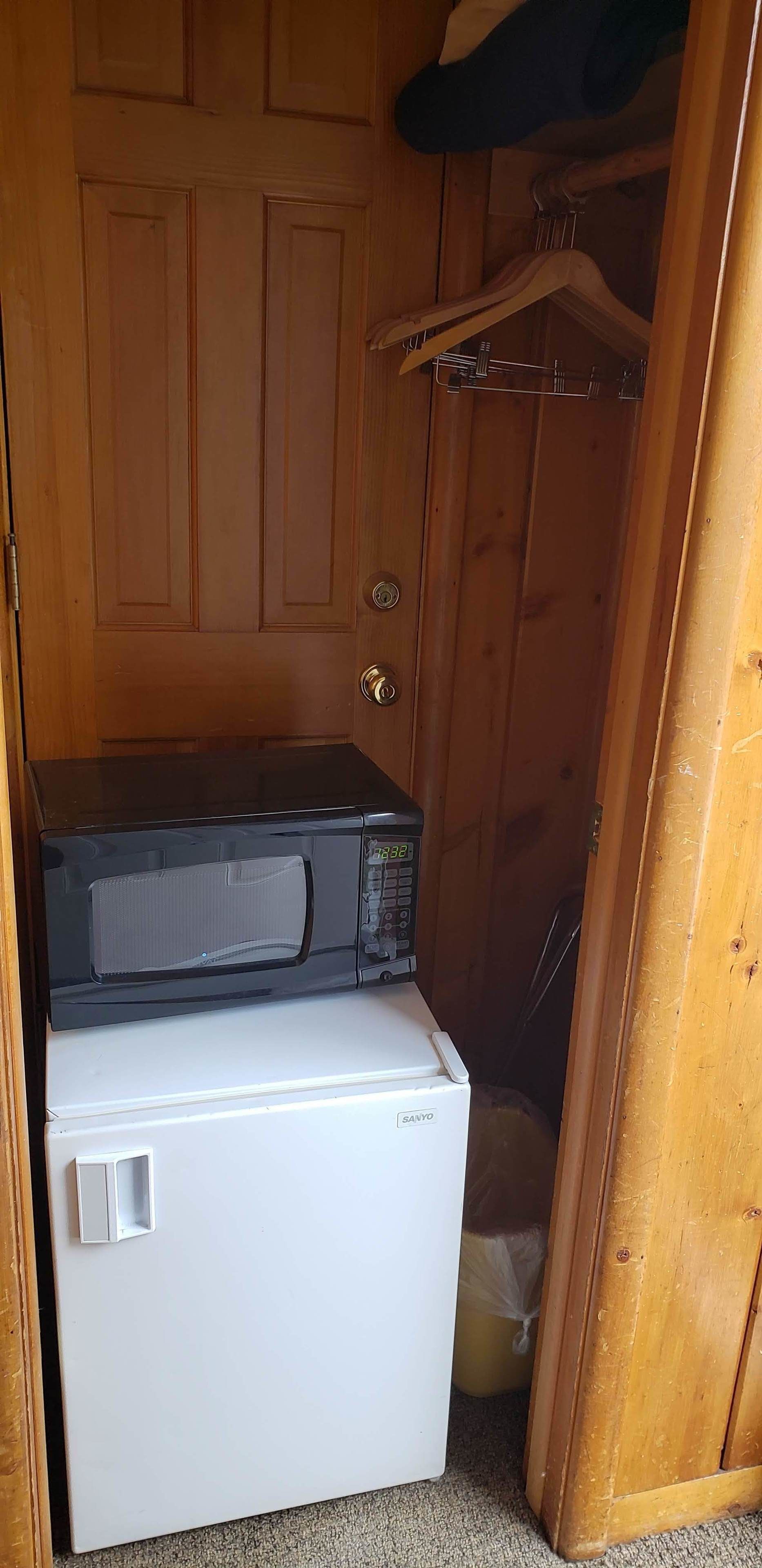 A compact room with a wooden door, a white refrigerator, and a black microwave on top.