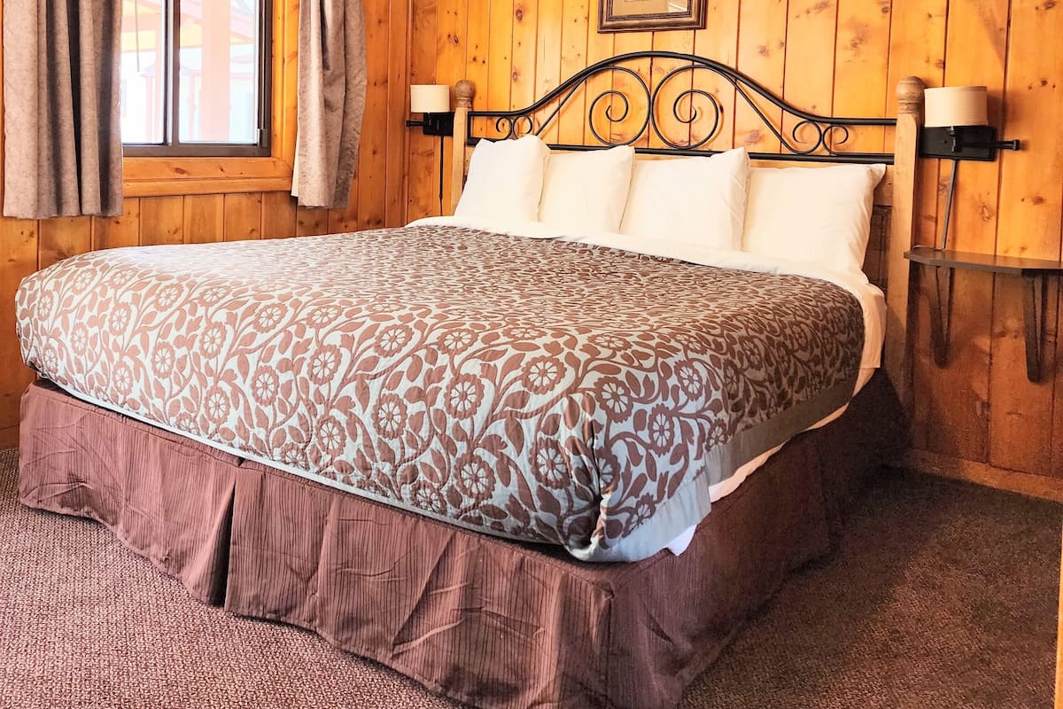 Ein Zimmer mit Holzwänden, einem Bett, Vorhängen, einem Fenster und Wandleuchten.