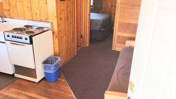 Een knus houten vakantiehuisje met een kitchenette, een enkel bed en een kleine badkamer.