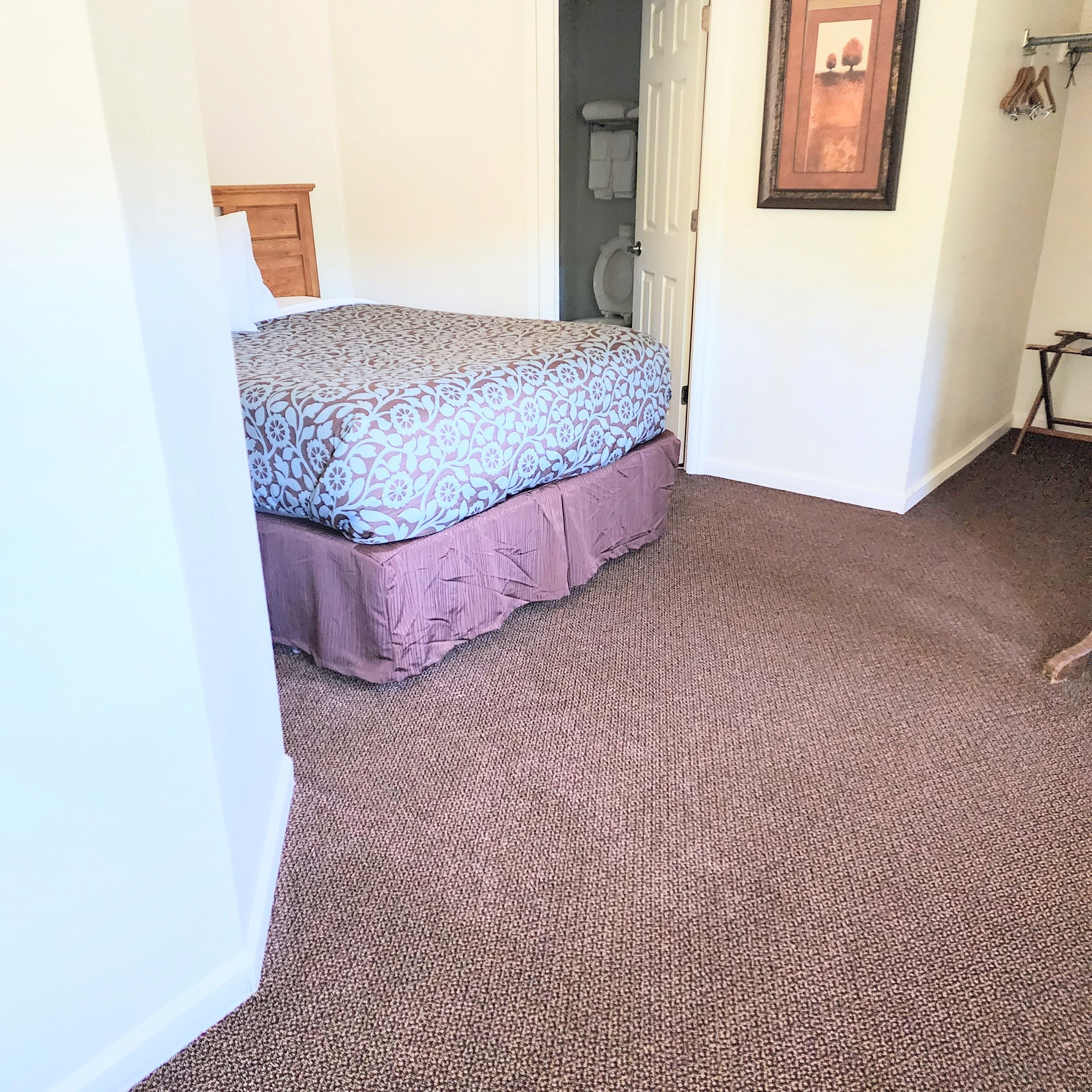Un dormitorio con cama, cabecera de madera, puerta e imagen enmarcada en la pared.