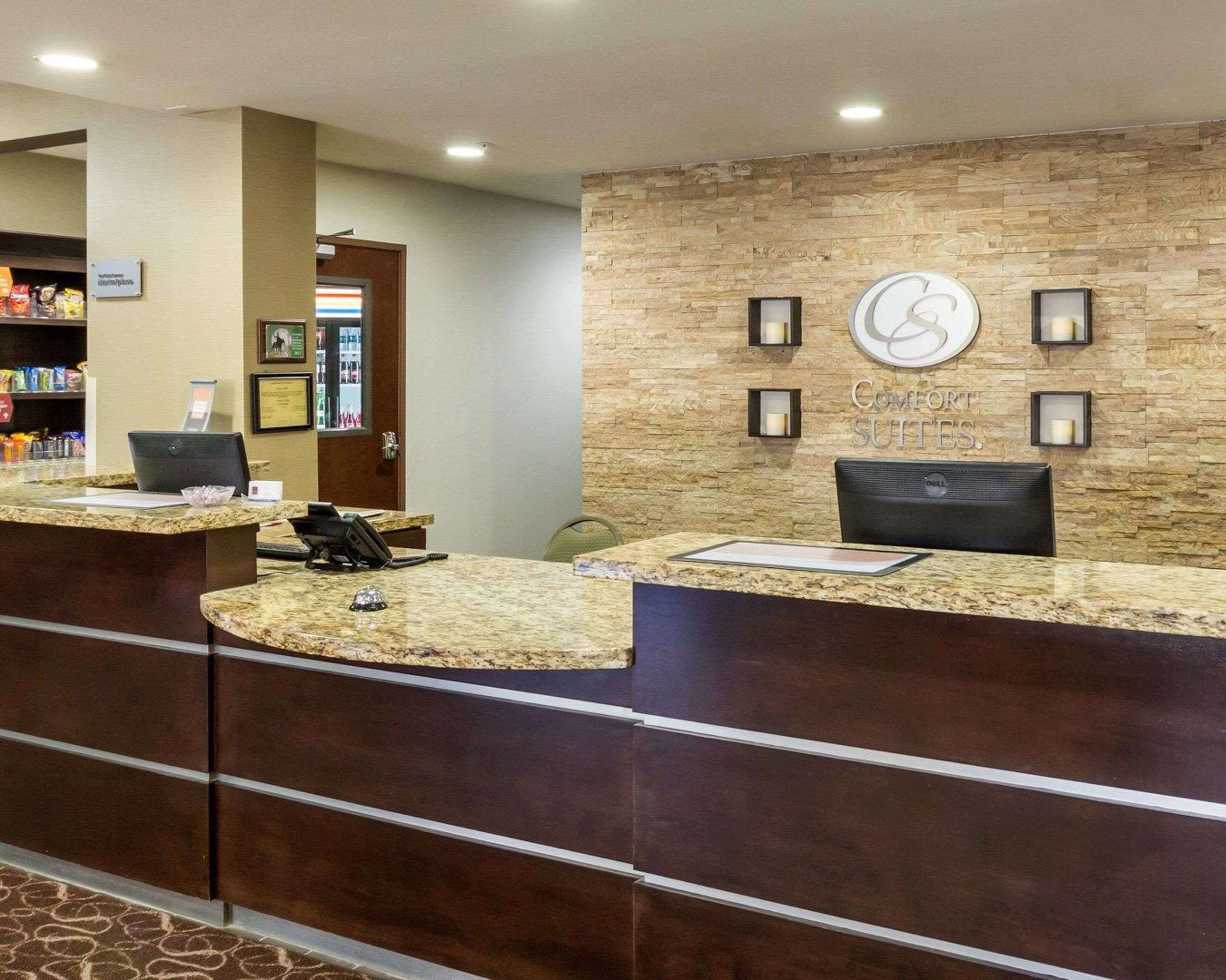 Zona de recepción de hotel con pared de piedra, mostrador de recepción y cartel de 'Comfort Suites'.