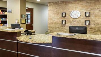 Zona de recepción de hotel con pared de piedra, mostrador de recepción y cartel de 'Comfort Suites'.