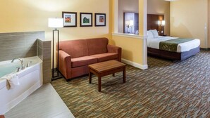 A hotel room with a bed, a sofa, a small table, a bathroom with a bathtub, and framed pictures on the wall. - Comfort Suites Cotulla near I-35 (Cotulla)