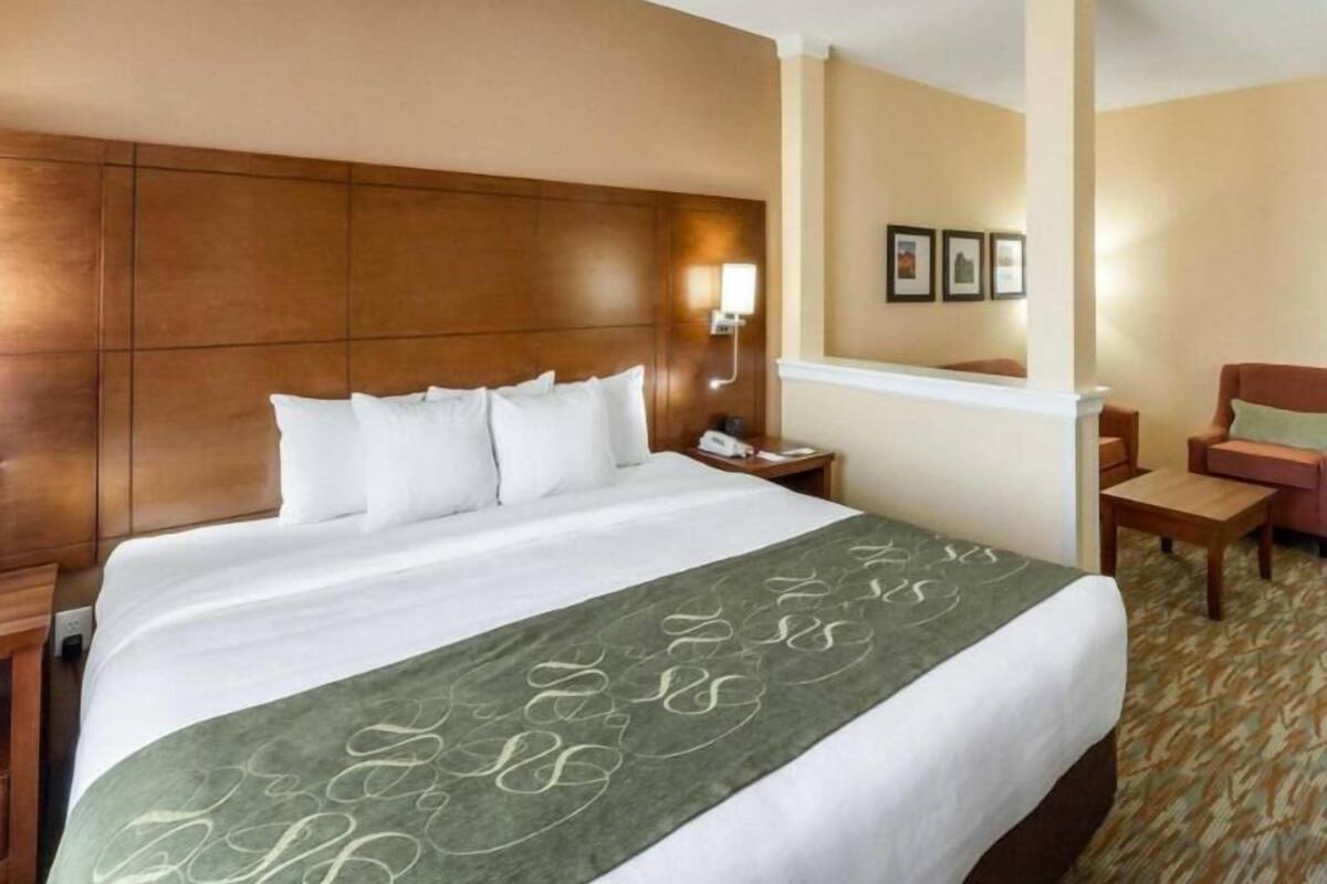 A hotel room with a large bed, a nightstand, a desk, a chair, and a wall-mounted lamp.
