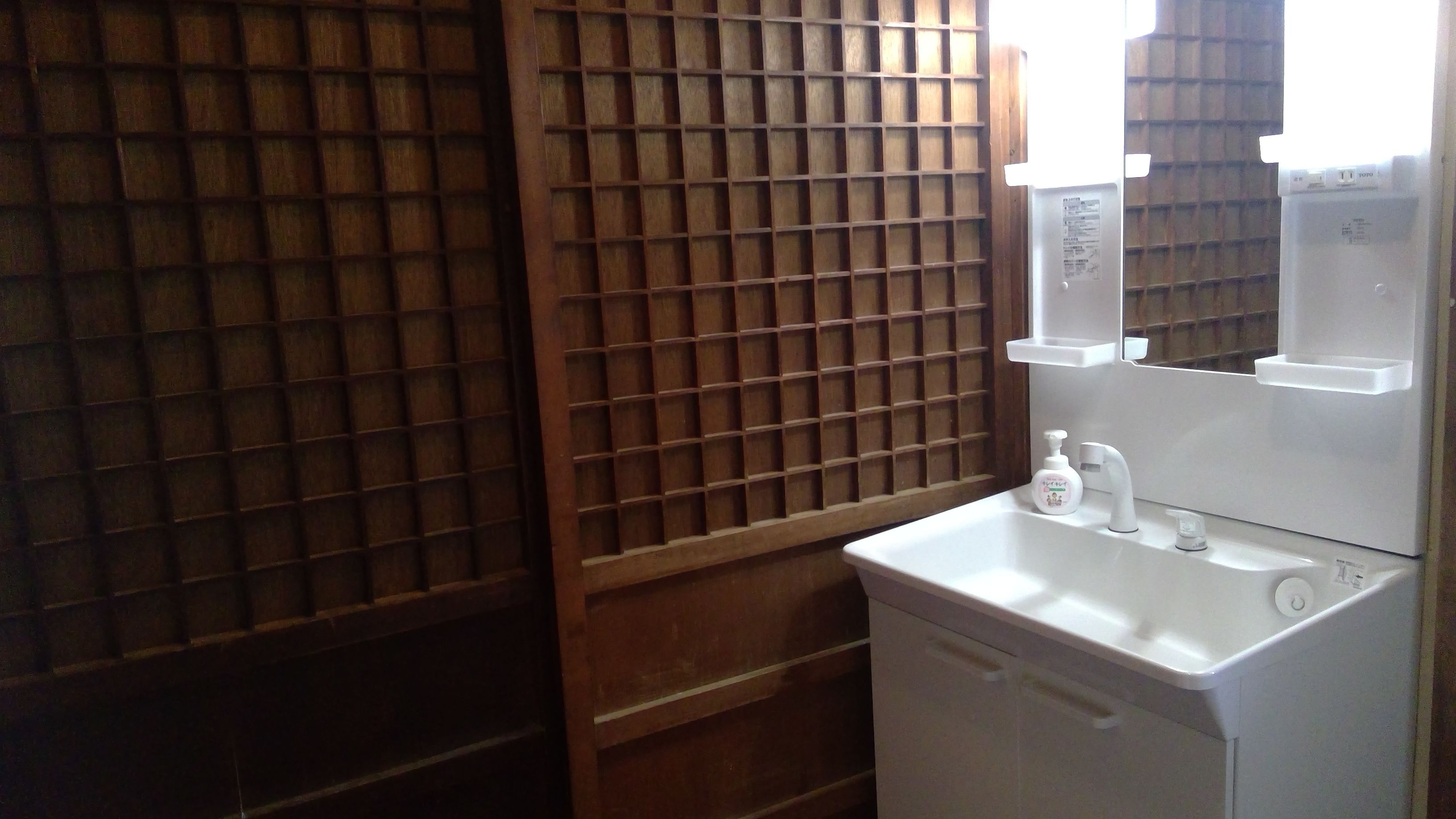 A bathroom with a white sink, a mirror, and a wooden lattice partition.