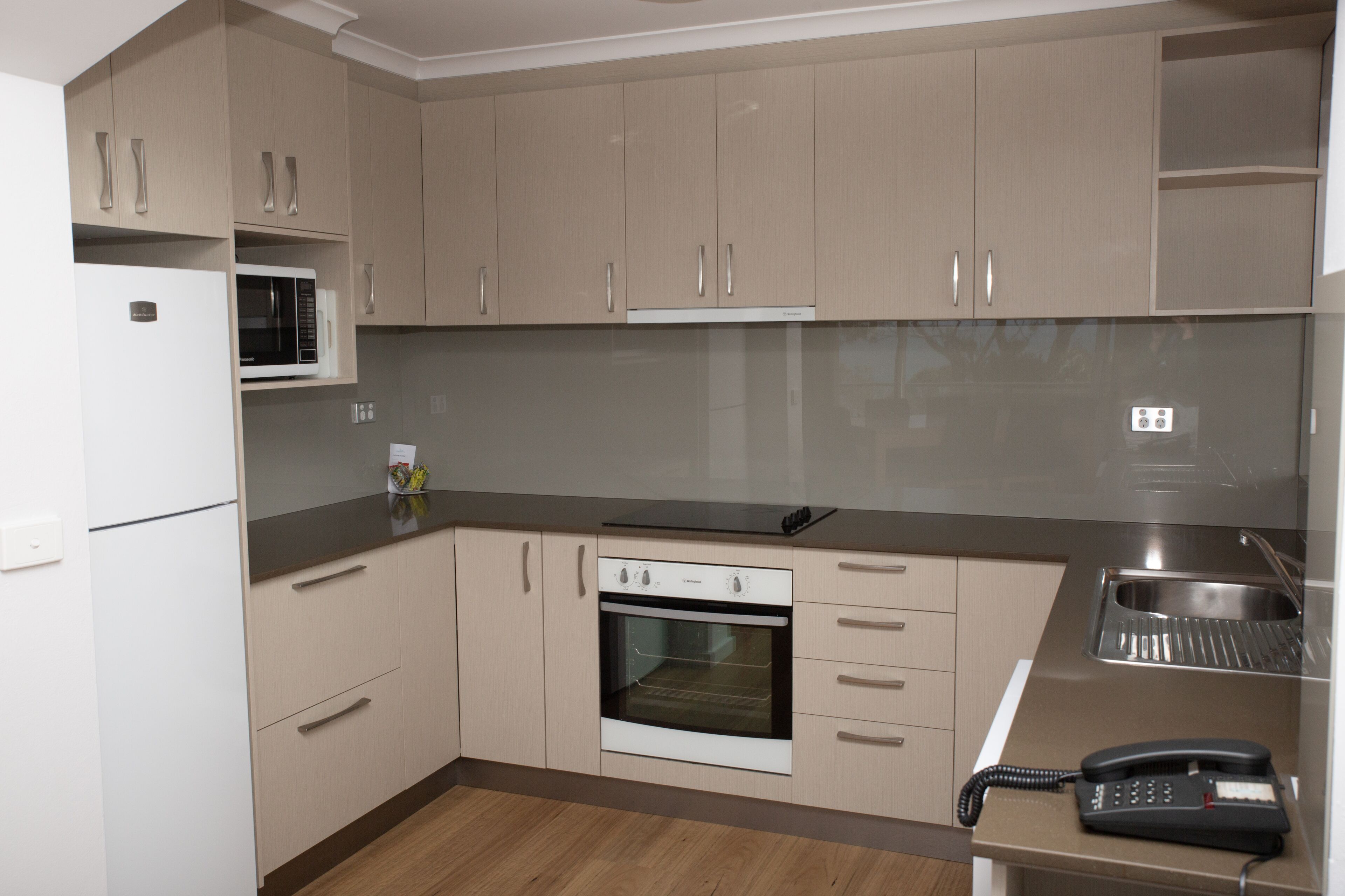 A modern kitchen with beige cabinets, a microwave, an oven, a sink, and a telephone.
