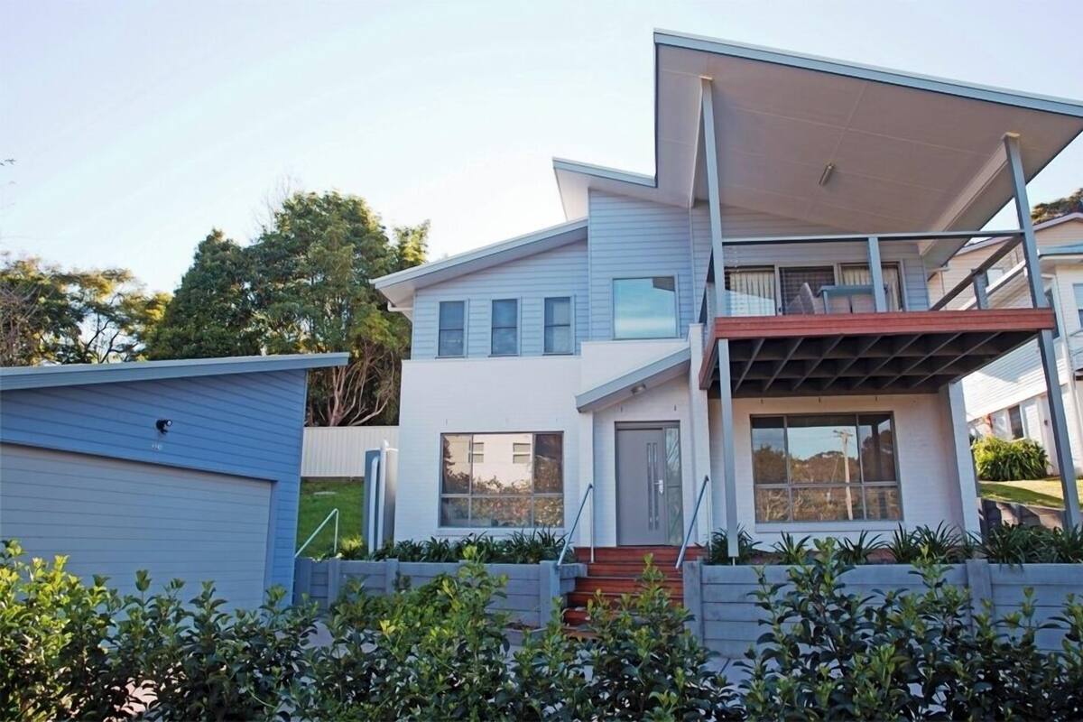 Ein modernes, zweistöckiges Haus mit Flachdach, großen Fenstern und einer überdachten Terrasse.