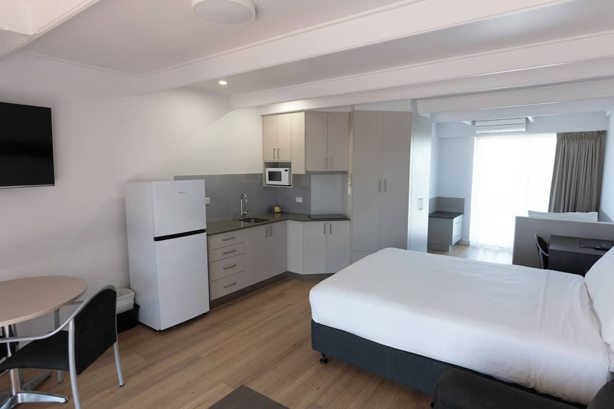 Ein modernes Hotelzimmer mit Bett, einer kleinen Küchenzeile, einem Essbereich und einem an der Wand montierten Fernseher.