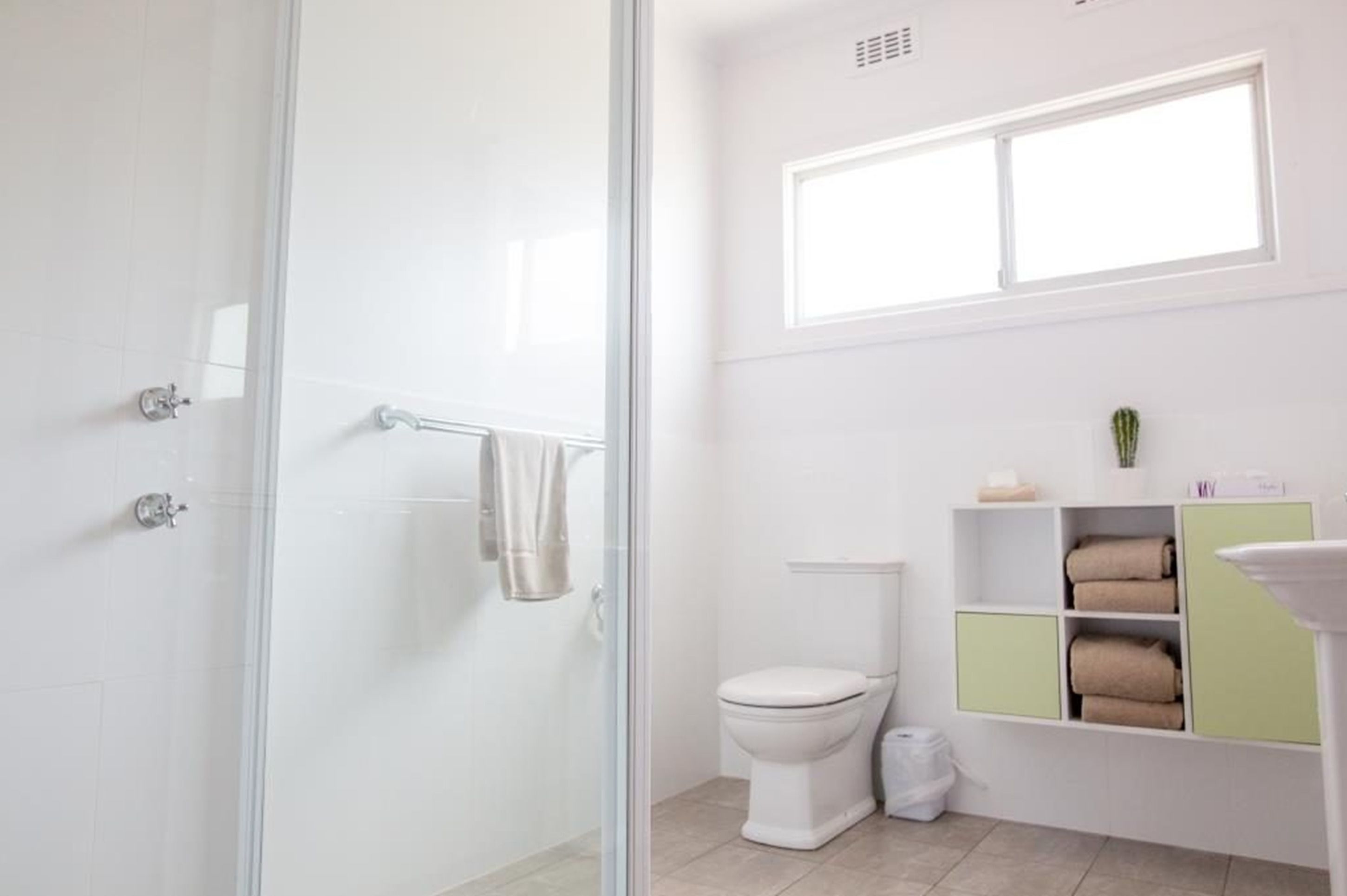 A modern bathroom with a glass shower enclosure, a toilet, and a vanity with shelves for towels.