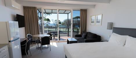 A hotel room with a bed, a desk, a chair, a sofa, and a balcony with a view.