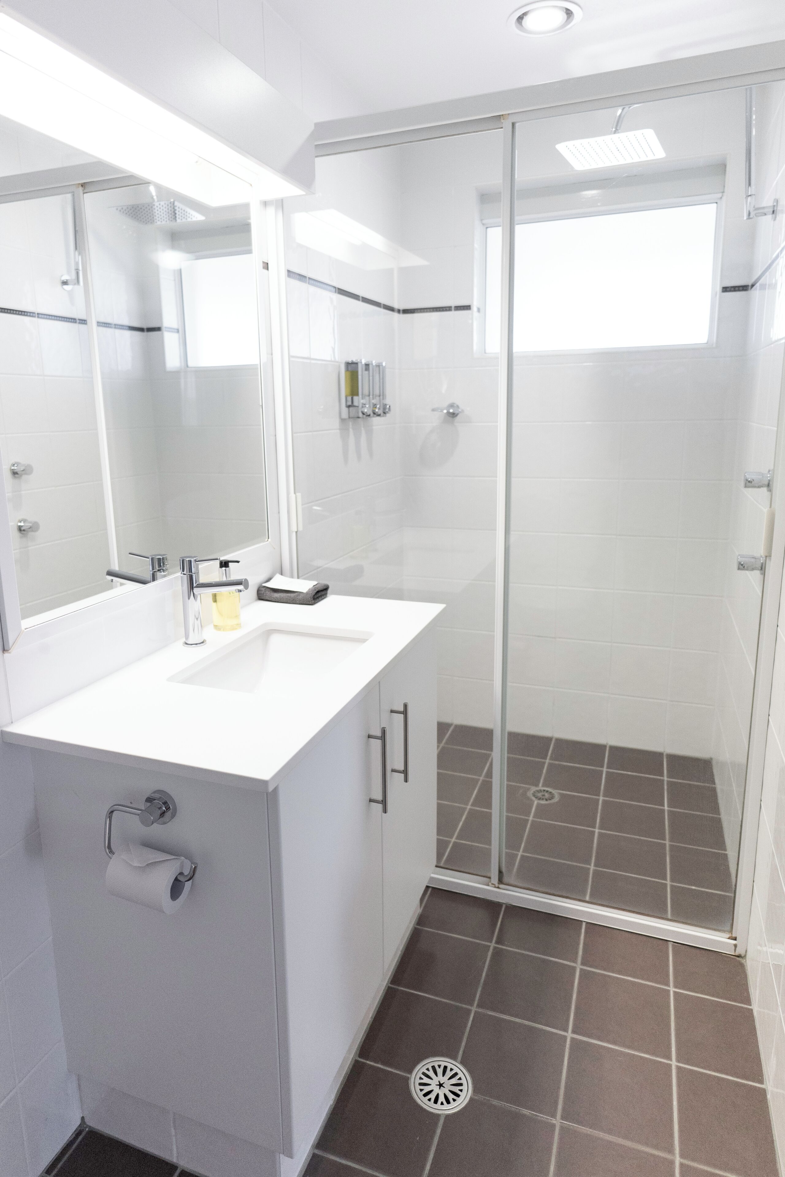 A modern bathroom with a white sink, mirror, and shower enclosure.