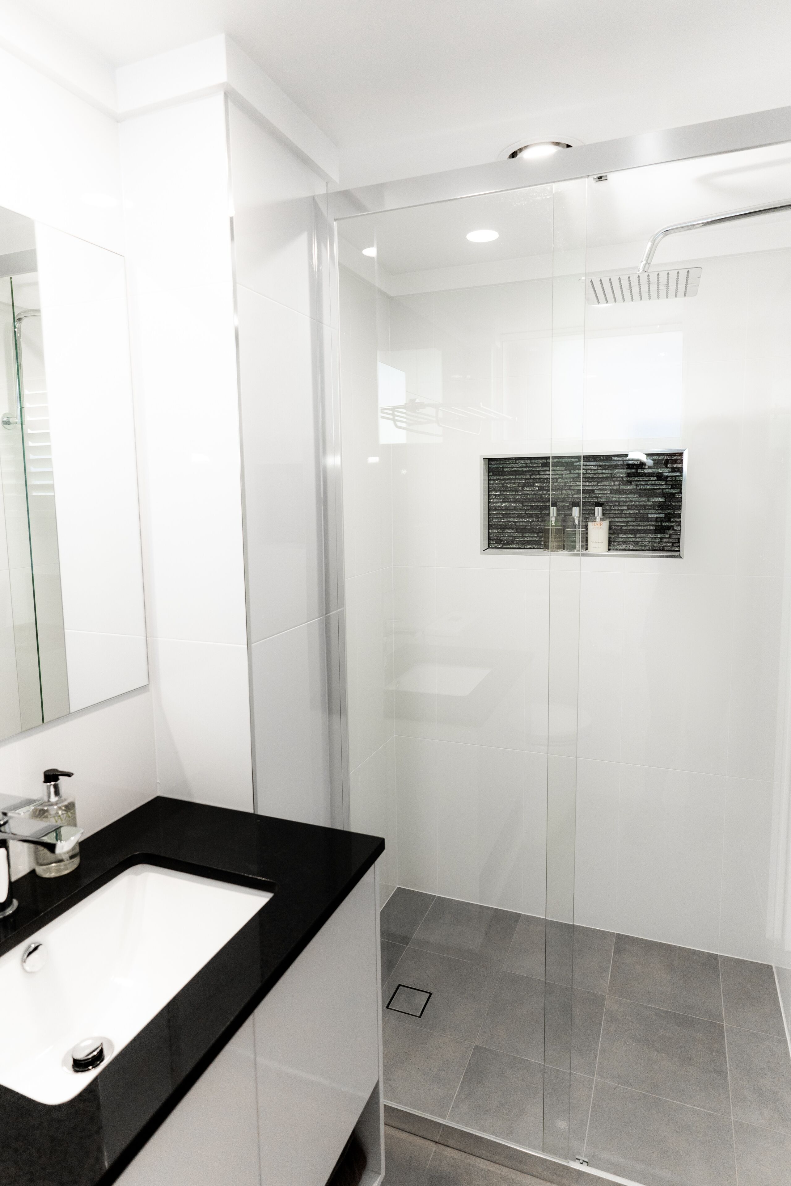 A modern bathroom with a black countertop sink, a glass shower enclosure, and a wall-mounted mirror.