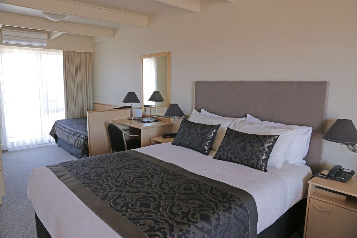 Ein Hotelzimmer mit einem großen Bett, einem Schreibtisch, einem Stuhl, einem Telefon und einem Spiegel.