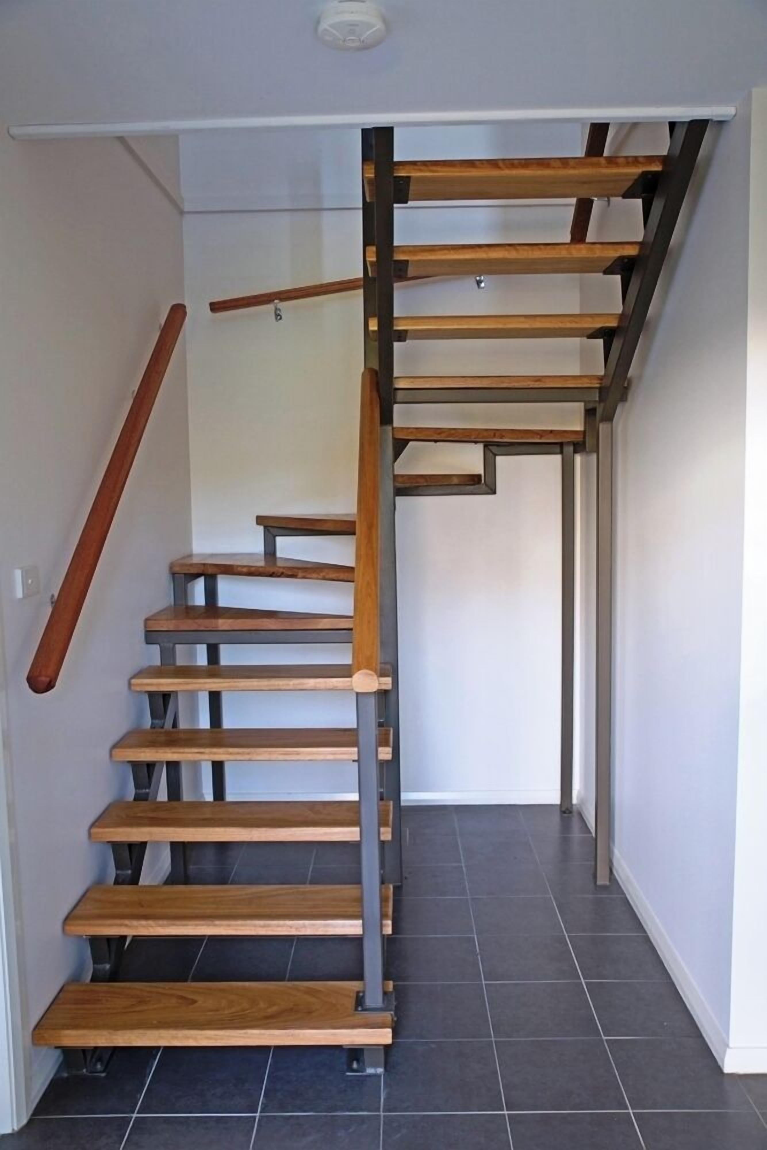 Una escalera moderna con escalones de madera y barandillas de metal, que conduce a un piso superior.