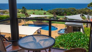 A pool area with a view of the ocean, a golf course, and a lounge area with a table and chairs. - Amooran Oceanside (Narooma)