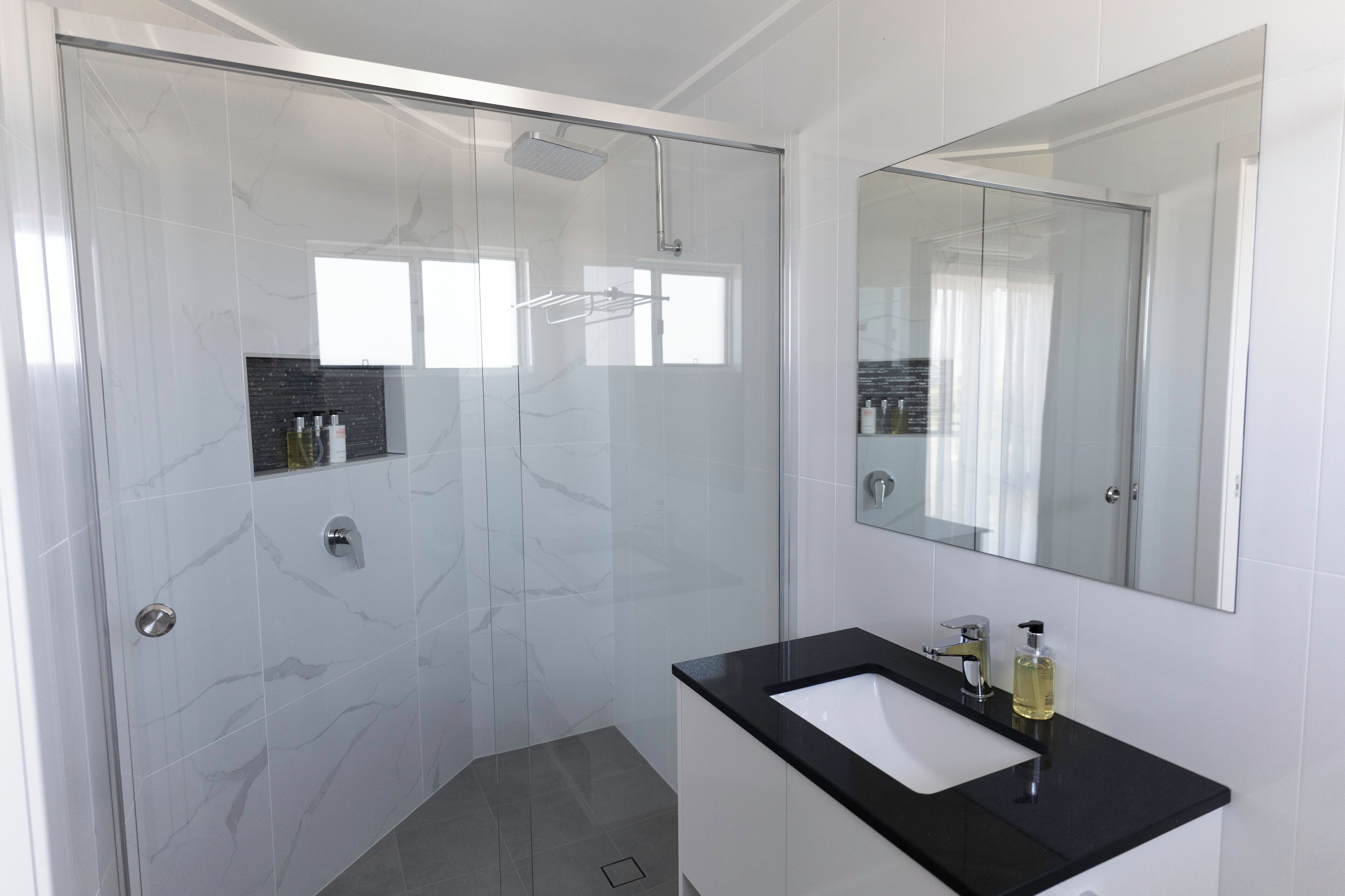 Un bagno moderno con doccia vetrata, lavabo su piano nero e uno specchio grande.