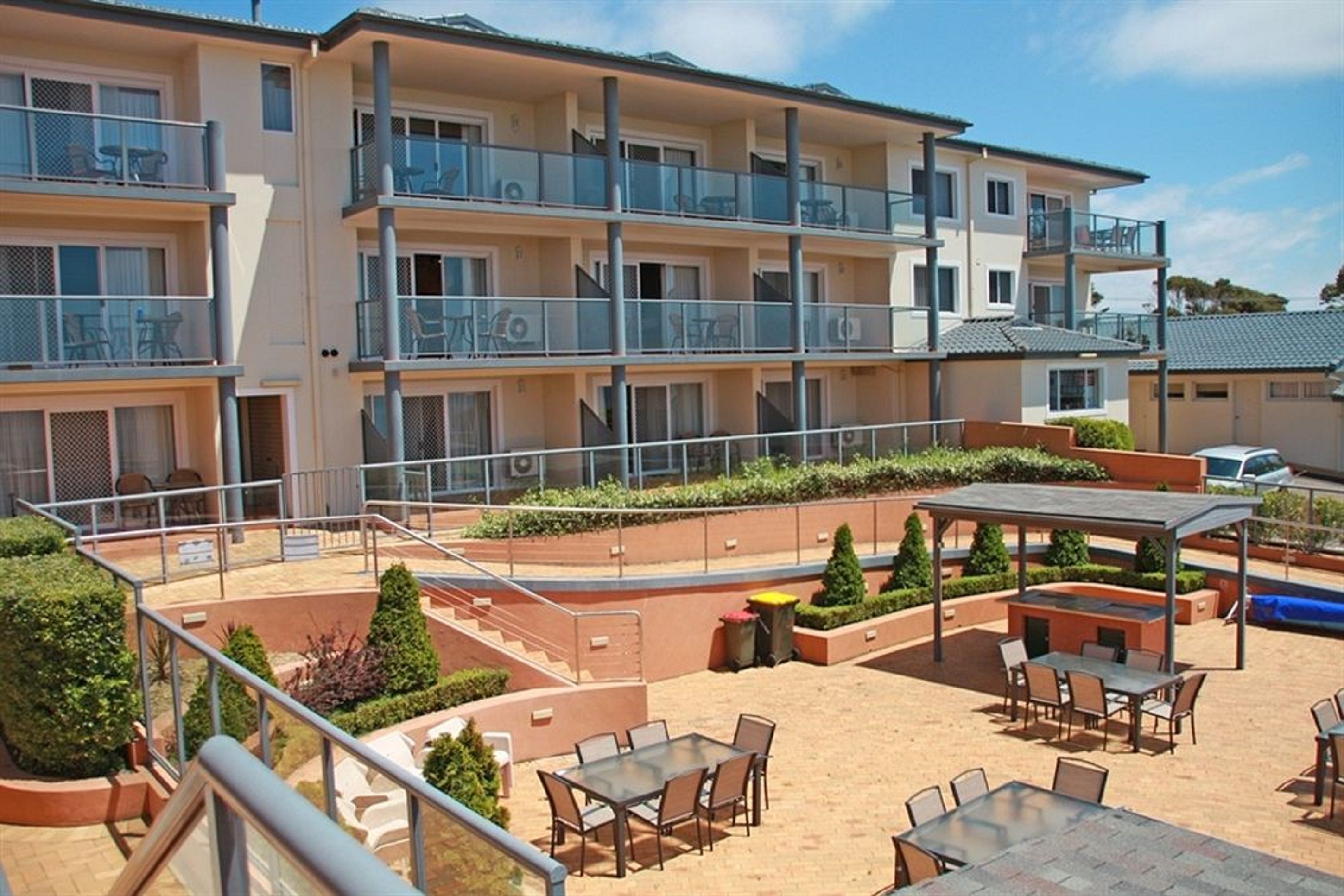 A multi-story hotel with outdoor seating areas, a covered patio, and a landscaped garden.