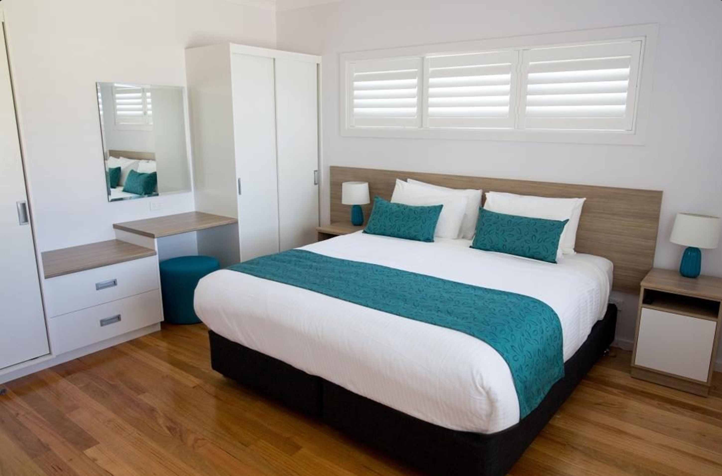 A bedroom with a bed, bedside tables, a wardrobe, a mirror, and a window with blinds.