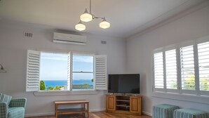 A living room with a large window, a flat-screen TV, wooden flooring, and a bench. - Amooran Oceanside (Narooma)