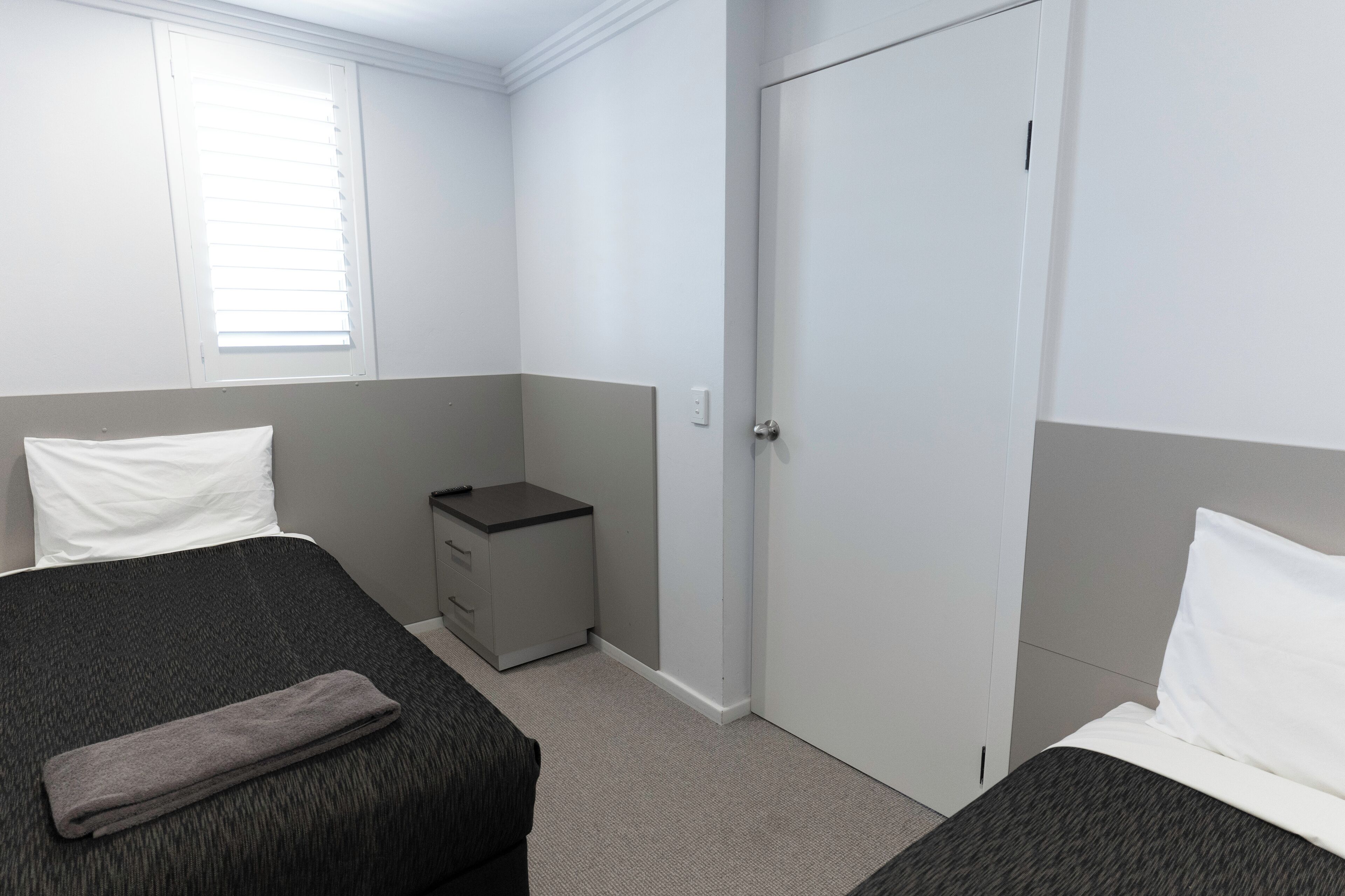 A hotel room with two beds, a wardrobe, and a small desk.
