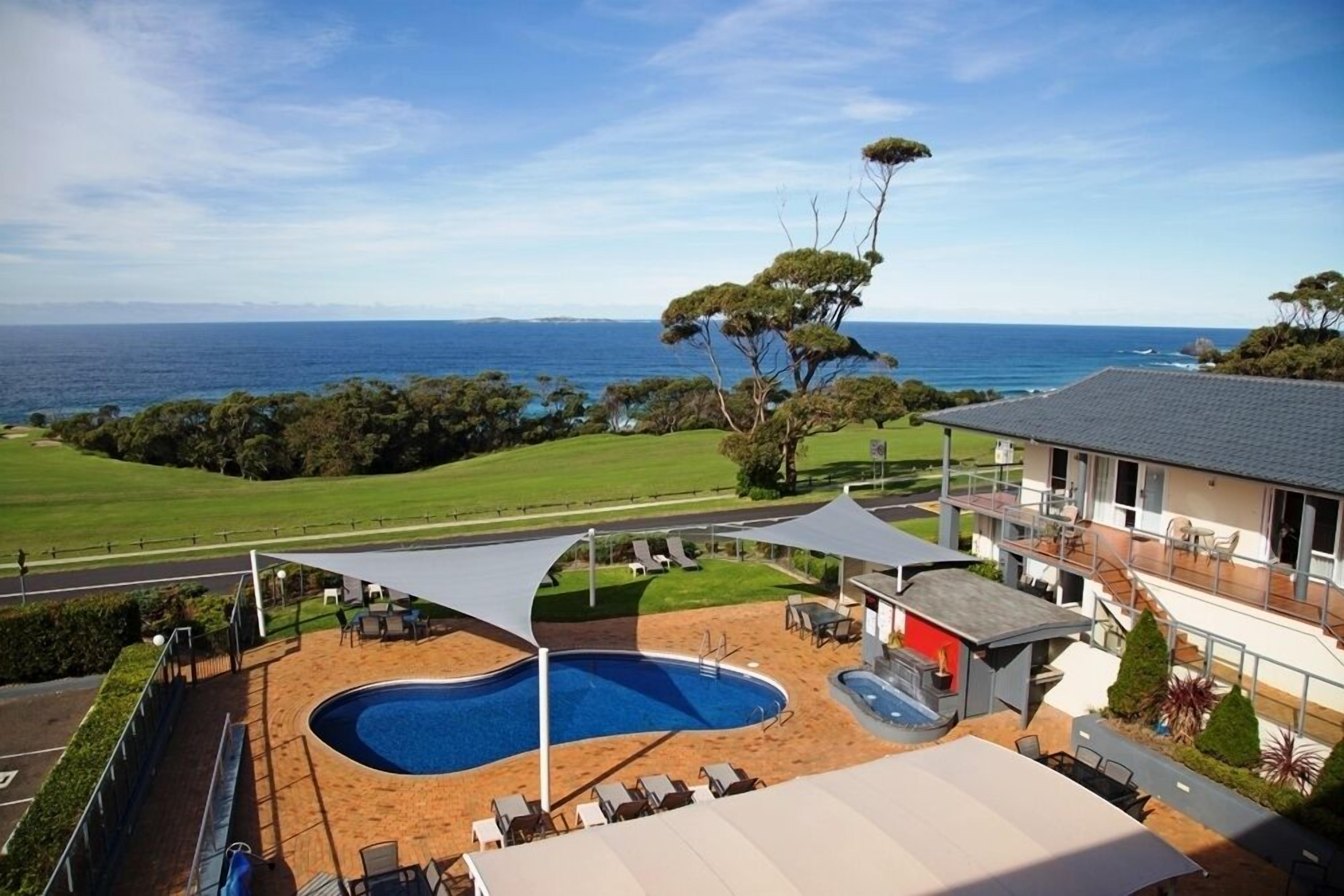 A pool area with a view of the ocean, surrounded by a deck and lounge chairs.