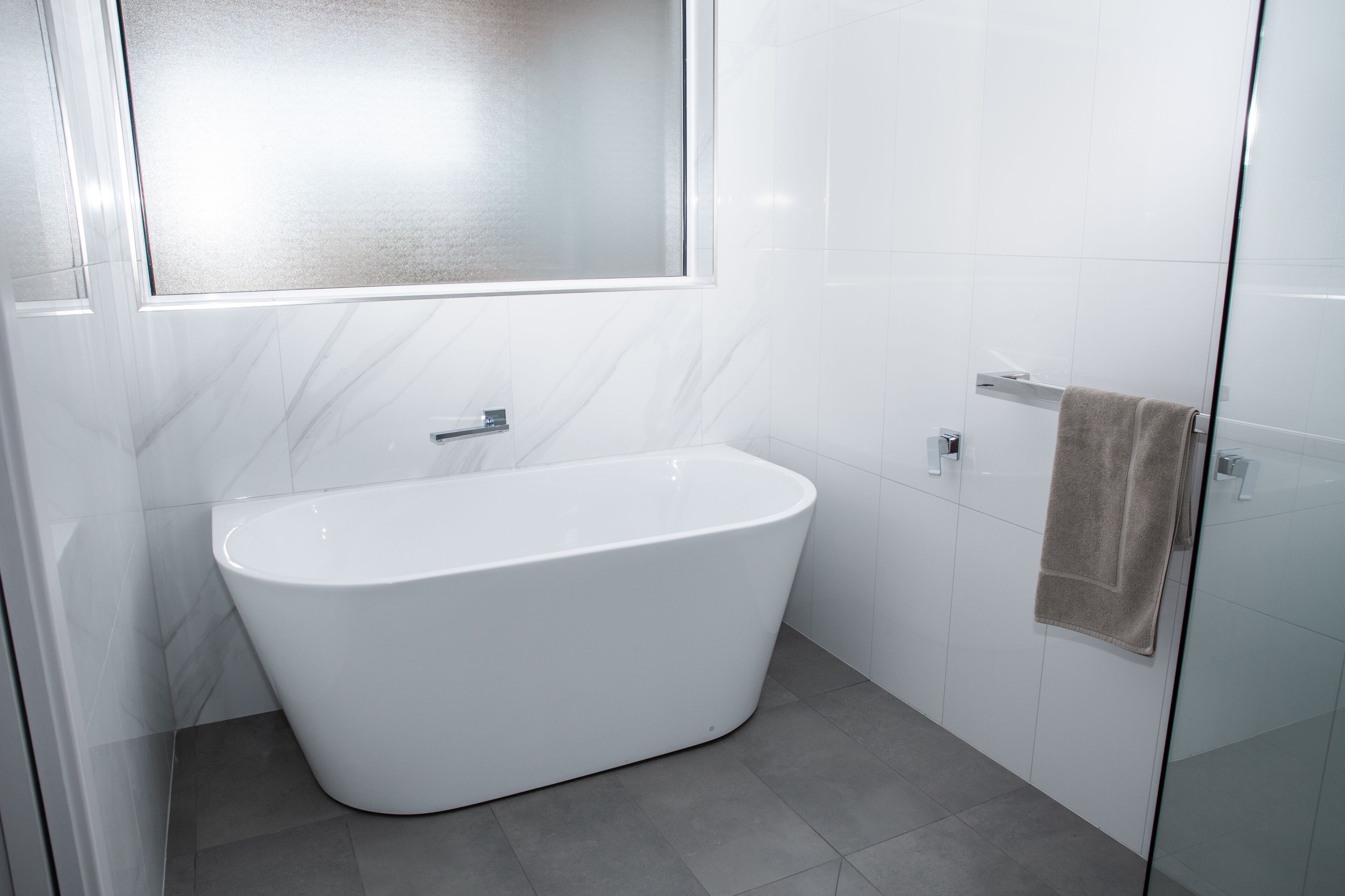 A modern bathroom with a freestanding bathtub, a glass shower enclosure, and a towel hanging on the wall.
