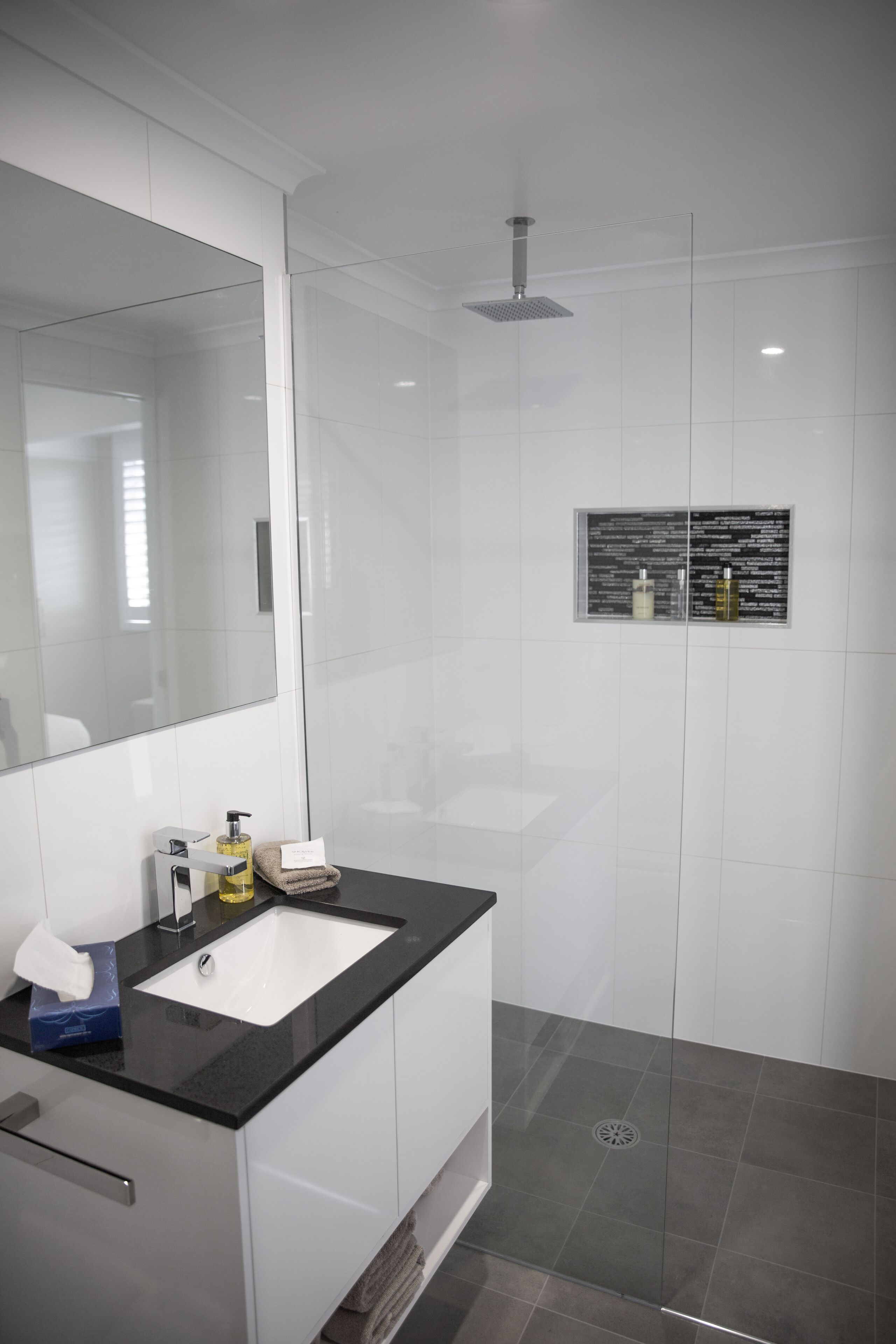 A modern bathroom with a large mirror, a black countertop sink, and a glass shower enclosure.