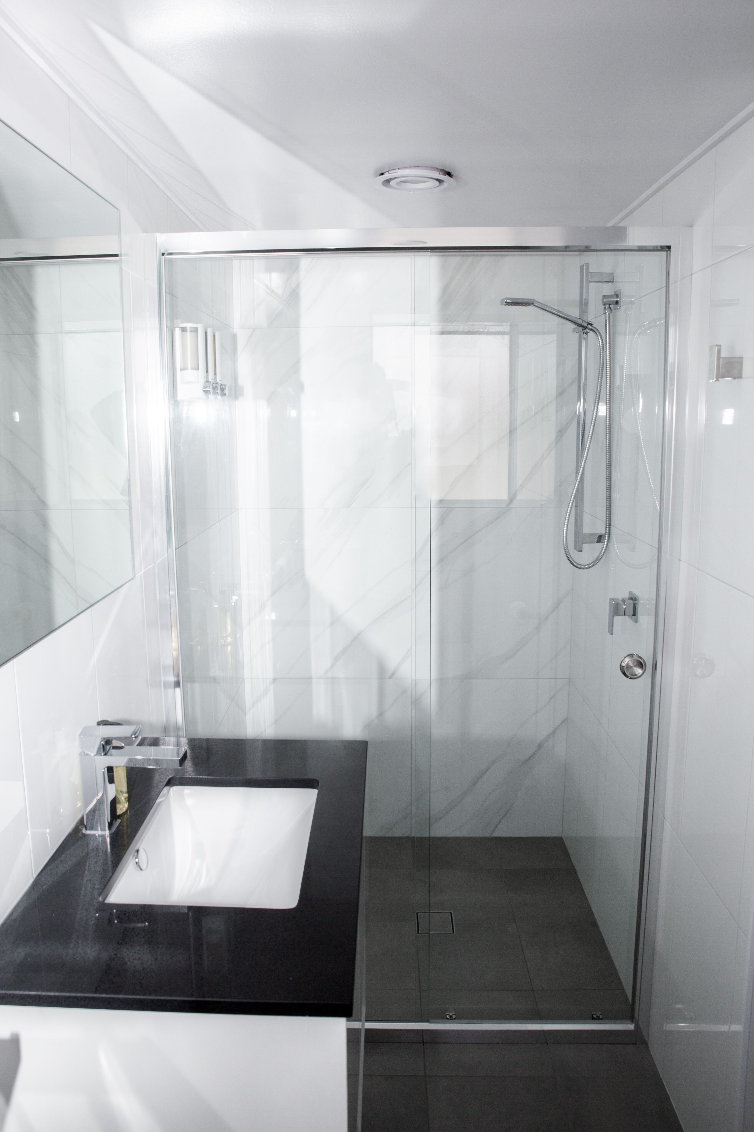 A modern bathroom with a glass-enclosed shower, a black countertop, and a white sink.