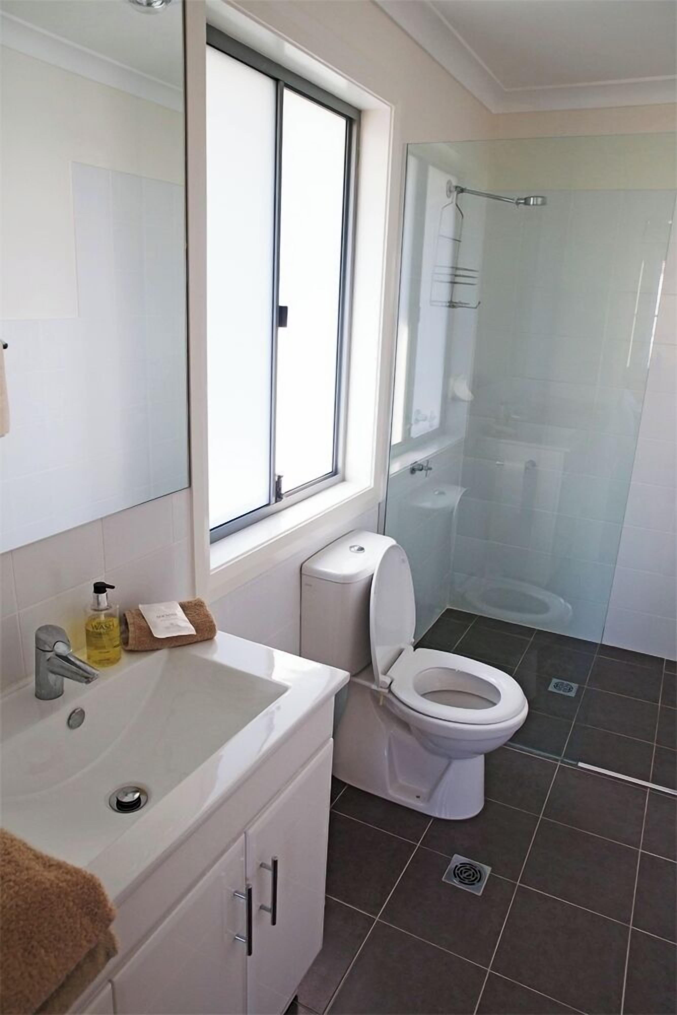 Une salle de bain moderne avec un lavabo blanc, des toilettes et une douche à parois de verre.