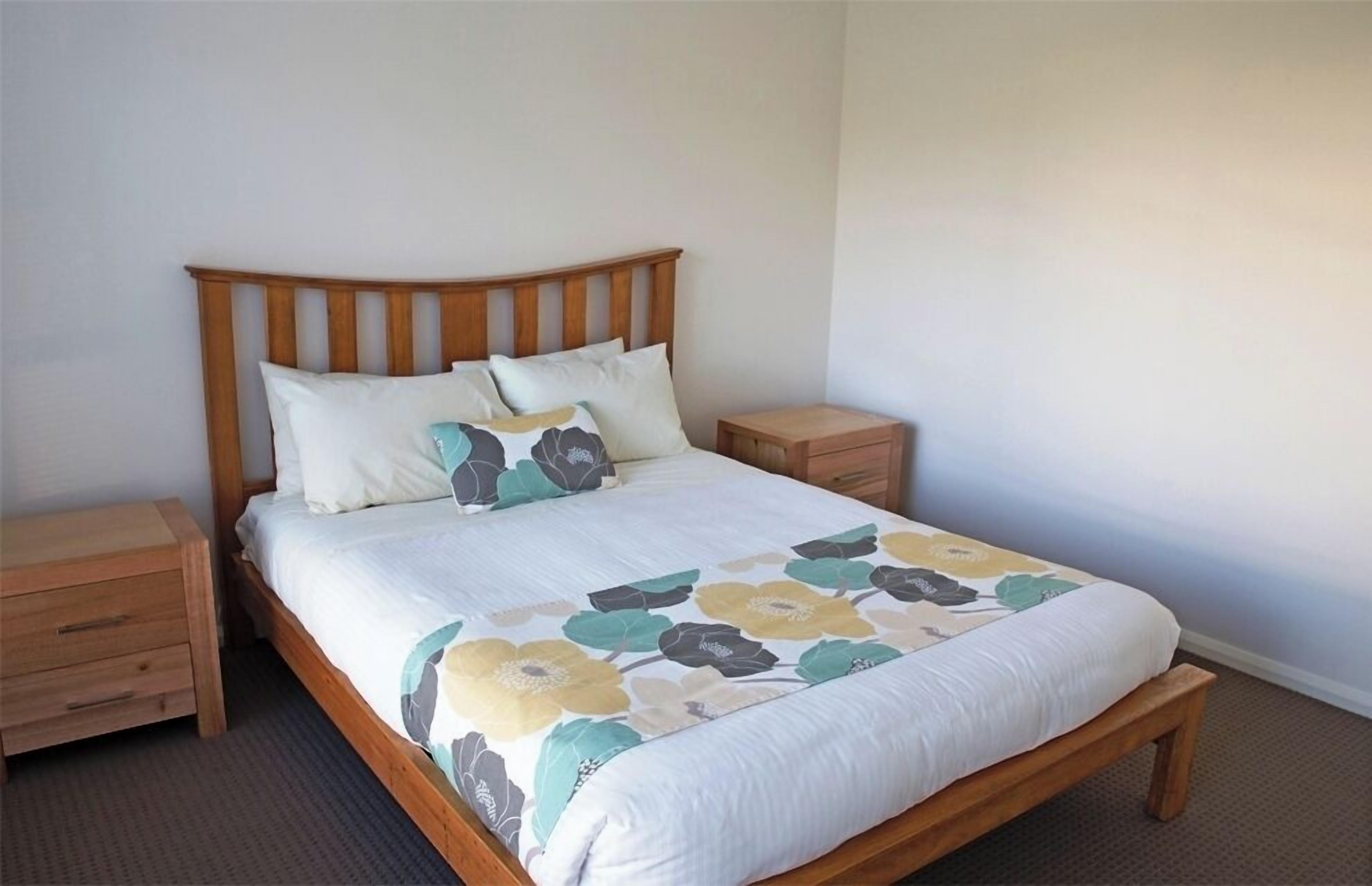Un lit bien fait, avec une couvre-lit à motifs floraux, une tête de lit en bois et des tables de chevet assorties.