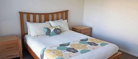 A neatly made bed with a floral bedspread, wooden headboard, and matching nightstands.
