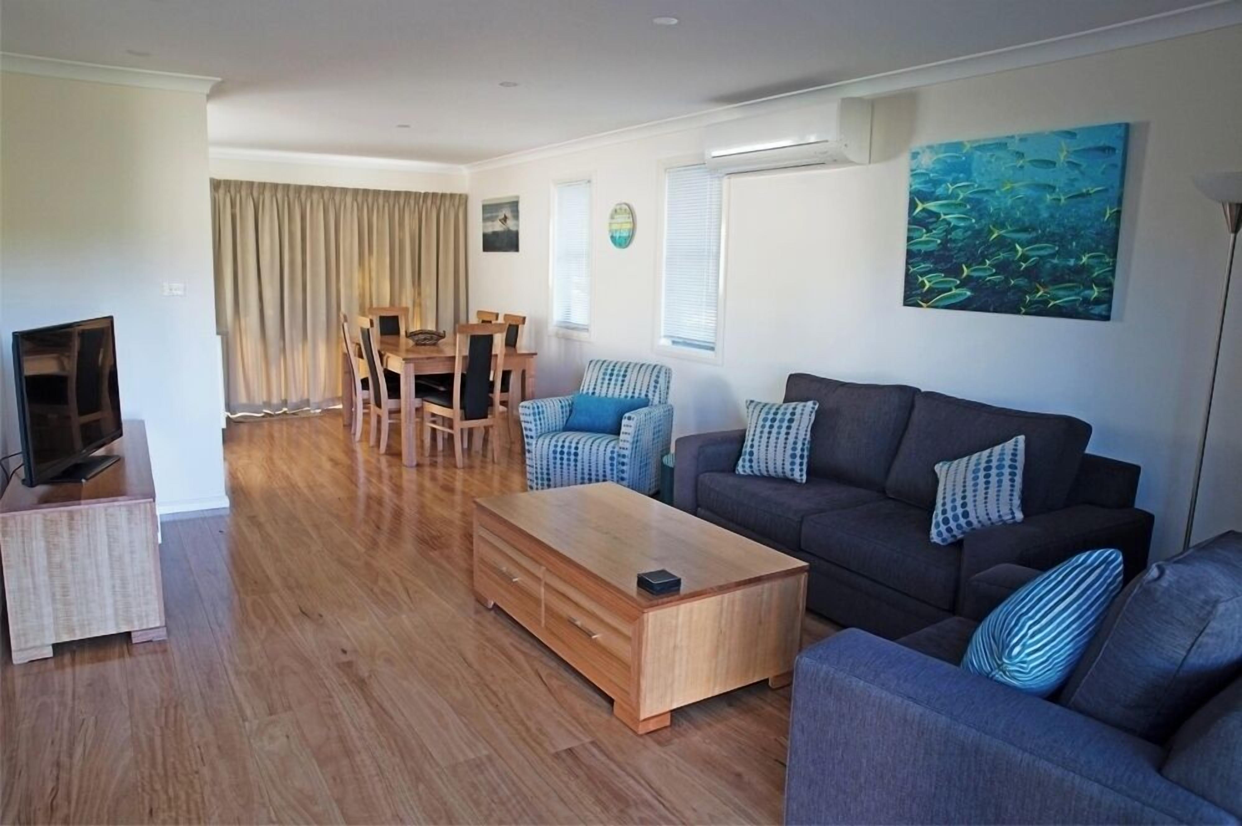 A modern living room with a wooden coffee table, grey sofas, and a dining area with a table and chairs.