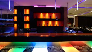 A modern bar area with illuminated shelves and a seating area with a colorful light display. - Miyana Hotel (Medan)