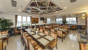 A spacious dining area with multiple tables and chairs, large windows offering city views, and a decorative ceiling design. - Chalcedony Grand Hotel (Hanoi)