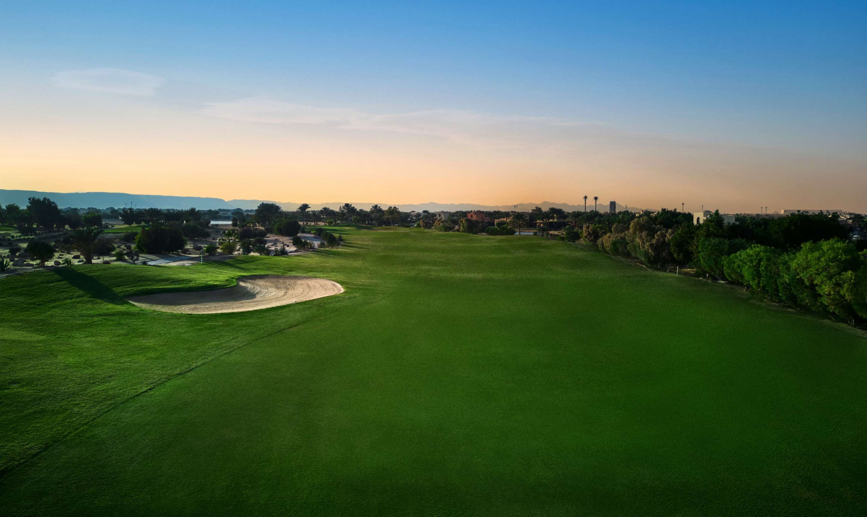 Un parcours de golf offrant une vue dégagée sur le green, les bunkers de sable et les arbres environnants.