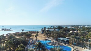 A resort with a swimming pool, palm trees, and a view of the sea.
