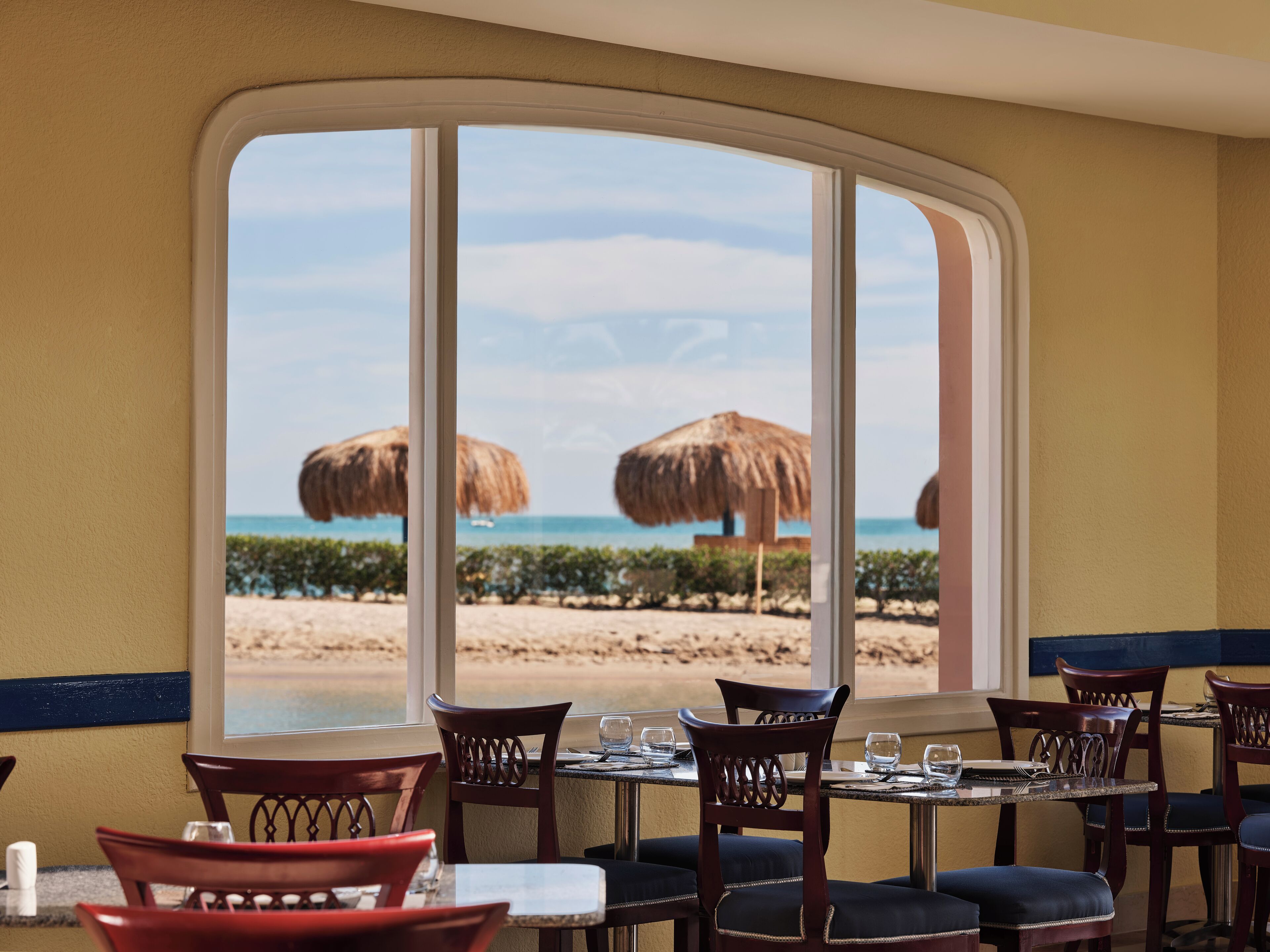 Un restaurant avec vue sur la plage, doté de tables et de chaises, et d’une grande fenêtre donnant sur l’océan.