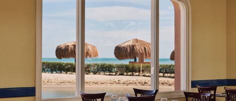 Un restaurant avec vue sur la plage, doté de tables et de chaises, et d’une grande fenêtre donnant sur l’océan.