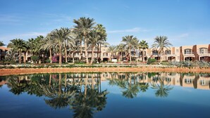 A resort with multiple-story buildings, palm trees, and a calm water body reflecting the structures.