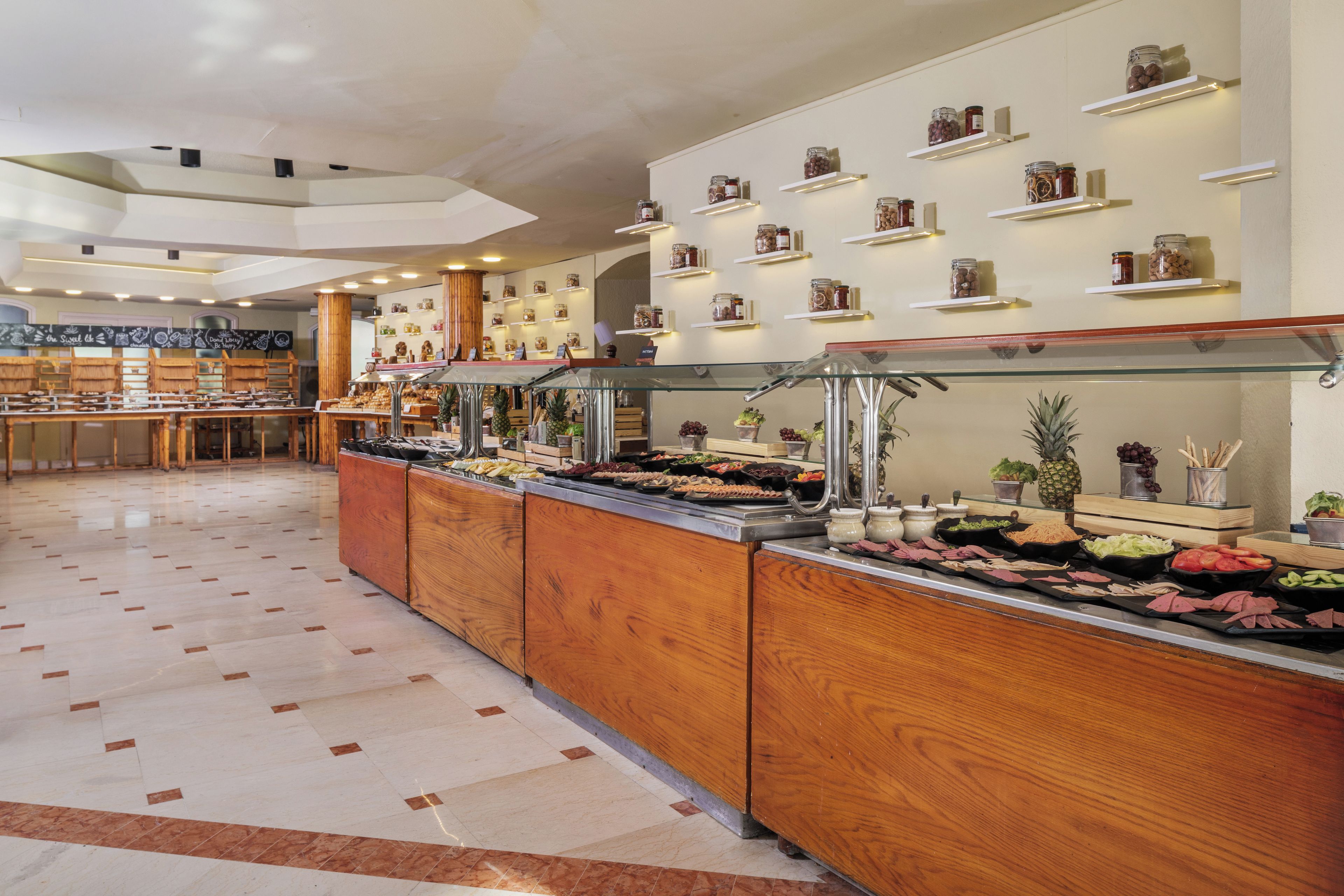 A buffet area with a variety of food options, including fruits, vegetables, and meats, displayed on wooden counters with glass covers.