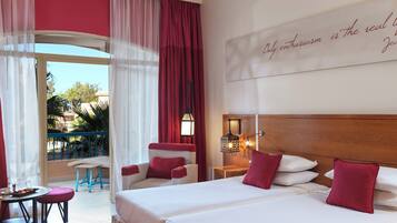 Habitación de hotel con dos camas, balcón, zona de comedor y vista a palmeras.