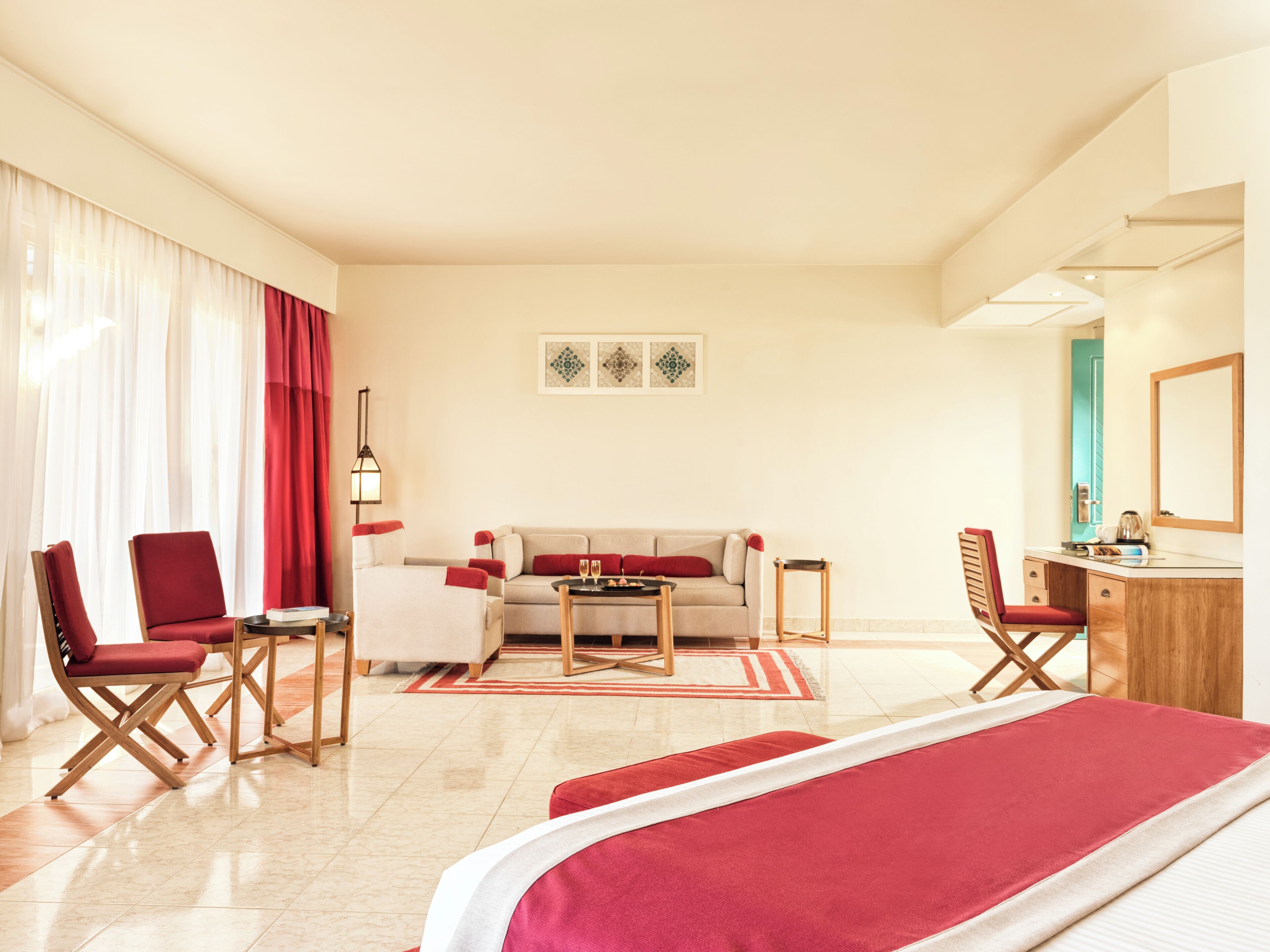A hotel room with a bed, two red chairs, a sofa, a desk, and a lamp.