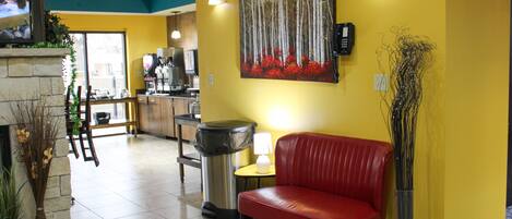 A reception area with a red sofa, a painting of trees, a trash bin, and a coffee machine in the background.
