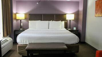 Habitación de hotel con una cama grande, dos mesitas de noche con lámparas, un banco y un aire acondicionado de pared.