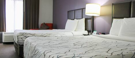 Une chambre d’hôtel avec deux lits, une table de chevet, une lampe et une fenêtre avec des rideaux.