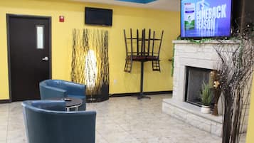 A lobby with a fireplace, a television mounted on the wall, and two blue armchairs.
